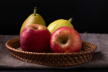Red apple and pear in basket on fabric with black background