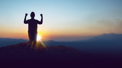 Silhouette of a person standing on a hilltop with arms raised in celebration against the sunrise...