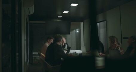 Diverse business team in serious discussion around boardroom table during meeting, using laptops...