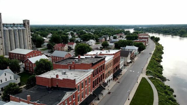 Aerial view of small riverside town with grain elevators near trees.