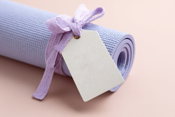 Purple yoga mat with blank tag and bow on pastel background