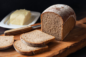 Square shape rye bread loaf cut into slices on old wooden cutting board, rustic style