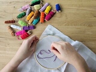 Hands creating a colorful embroidery design with thread on fabric during afternoon craft session concept