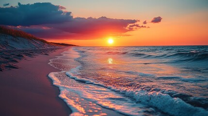 Vibrant sunset over ocean beach with waves gently lapping the shore.