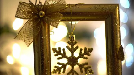 Gold snowflake ornament hangs in frame with bokeh background for holiday, greeting card or invitation