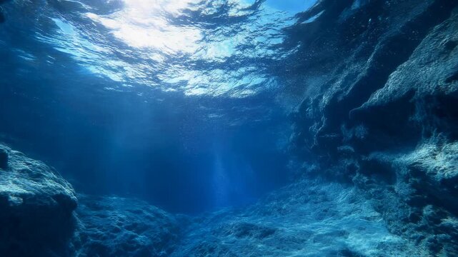Deep Underwater Cave View with Sun Rays, Surface Ripples, and Rising Air Bubbles