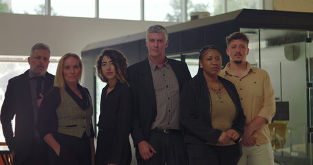 Obraz premium Diverse group of six professionals standing in modern office, serious expressions, business team posed together for group portrait in bright corporate environment