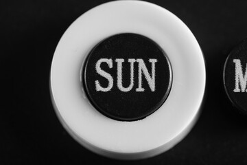 Close up view circular button labeled SUN on minimal calendar display, emphasizing texture and simple monochrome style.