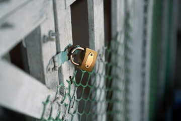 A closeup of a simple golden lock used to lock a white wooden gate to a house