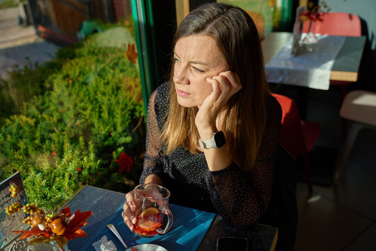 Woman drinking tea by window in cafe in sunlight
