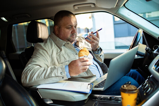 Adult man focused, multitasking with laptop and phone in car