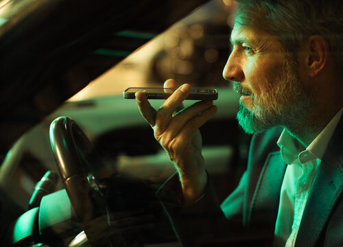 Focused mature man using voice command on smartphone in car at night