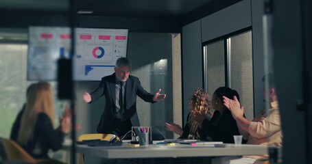 Diverse team applauding business leader following successful data presentation in modern corporate boardroom with screen displaying charts