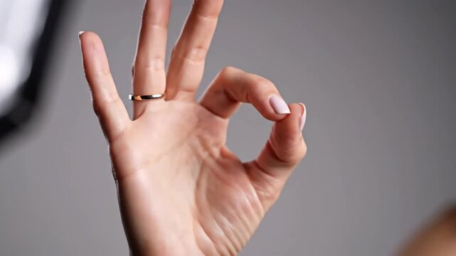 Woman's hand displaying the ok sign with a gold ring against a neutral background conveying approval and satisfaction in a studio setting with soft lighting and focus