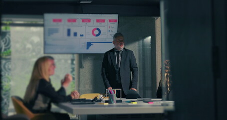 Diverse team applauding business leader following successful data presentation in modern corporate boardroom with screen displaying charts