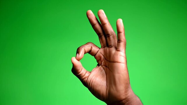 Darkskinned hand making the ok gesture against a vibrant green background symbolizing approval agreement and positive affirmation in a simple yet powerful visual statement