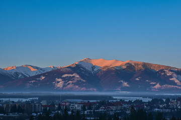 Snow-capped peaks of the Western Tatras Baranec Mountains bathed in golden alpine light at sunrise and a city hidden in the valley below