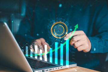 A person interacts with a laptop, Holographic display featuring a bar graph and an upward-trending line graph, symbolizing business growth and data analysis. Suggesting performance metrics or targets