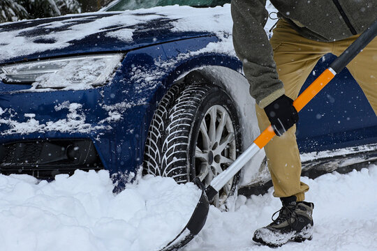 Person shoveling snow from around a car's wheel, facing winter challenges and needing assistance