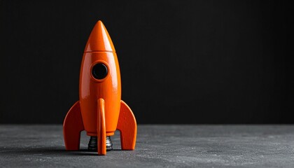 Orange Toy Rocket Standing Upright on Dark Surface with Black Background
