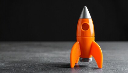 Orange Toy Rocket Standing Upright on Dark Surface with Black Background
