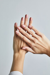 Woman&rsquo;s hand with soft pink manicure and a delicate diamond band ring, posed against a neutral grey background