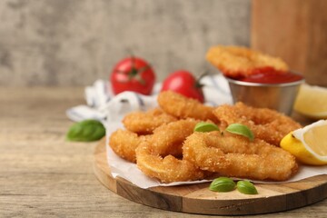 Deep fried squid rings with lemon slice, basil and ketchup on wooden table, closeup. Space for text