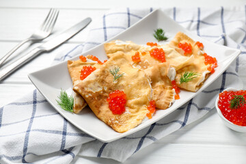Delicious crepes with red caviar and sour cream served on white wooden table, closeup