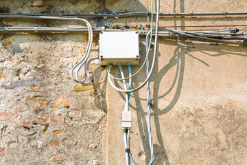 Electrical and telephone cables with plastic junction box against an old plaster wall