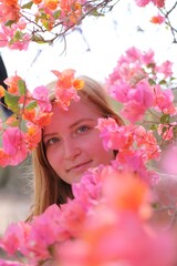 Woman gently smelling bright bougainvillea flowers outdoors on a sunny day, enjoying a calm and...