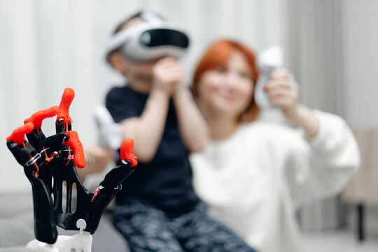 Closeup toy robotic arm made by 3D printer, Young caucasian child with vr headset with adult female in background