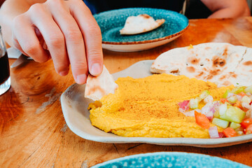 a man lifts naan with curry hummus at a restaurant