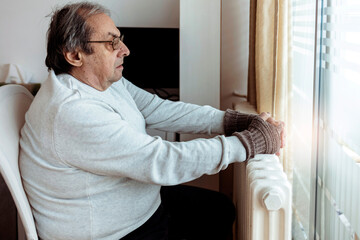 Energy crisis, man feels the cold next to the radiator. Sad man sitting by the window next to the...