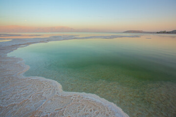 Abstract, high-contrast view of the Dead Sea shoreline, featuring intricate, crystalized white salt formations meeting the strikingly unnatural green water