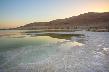 Abstract, high-contrast view of the Dead Sea shoreline, featuring intricate, crystalized white salt formations meeting the strikingly unnatural green water