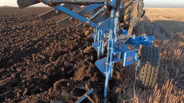 Tractor with agricultural machinery cultivates the arable land and prepares the soil for planting crops. Close up of a tractor plowing the land. The plow cuts the soil and turns it over, slow motion