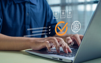 person working on a laptop with digital checkmarks and ISO icons, representing quality assurance, compliance, standards certification, auditing processes, and professional document verification.