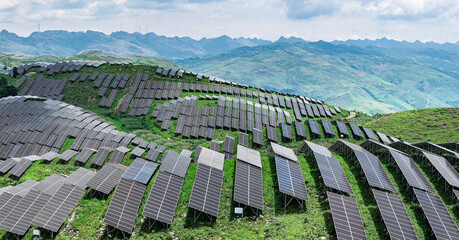 Solar panels and wind turbines on green mountain generating clean electricity.
