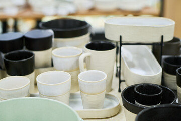 Ceramic cups, bowls, and plates arranged on table, showcasing various shapes and sizes of handmade tableware, highlighting craftsmanship and modern minimalist design