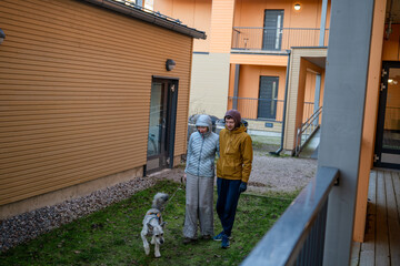 couple walking dog together in modern residential courtyard on cold autumn day