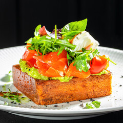Gourmet avocado toast with smoked salmon, fresh greens, cherry tomatoes and a poached egg served on crispy brioche bread