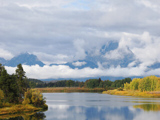 Close view of Snake River bend reflecting dense forest and heavy Teton cloud cover
