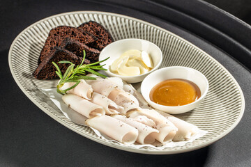 Elegant cold meat platter with thin turkey slices, dark bread, garlic and honey mustard sauce served on a modern plate, perfect for restaurant menus, catering advertising and gourmet food promotions