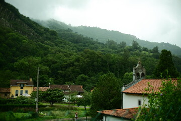 Mountain landscape with traditional village houses and a small church surrounded by lush green vegetation, located in the Asturias region of Northern Spain