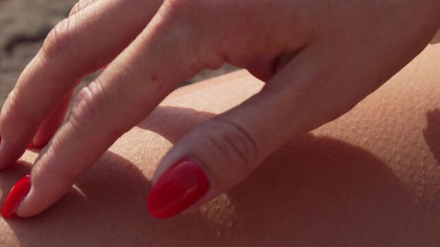 Hand skin touch, a woman's manicured hand with red nails gently touches and presses bare skin in a close-up shot