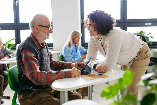 Senior man learning digital skills with tutor support in community center.