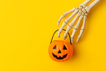 Skeleton hand holding a small pumpkin candy bucket