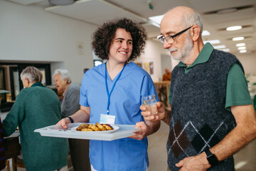 Senior man having lunch with supportive caregiver in community center cafeteria.
