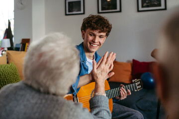 Young musician volunteer playing guitar for senirors in retirement home.