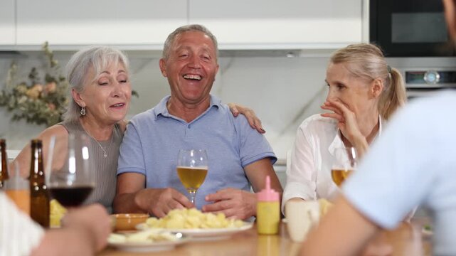 Cheerful mature men and women having jolly conversation with goblets in hands during lunch time